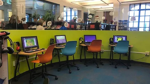 a colourful computer room for kids, with orange and blue chairs and a lime green wall against which are multiple computer screens.
