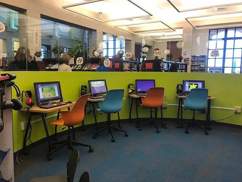 a colourful computer room for kids, with orange and blue chairs and a lime green wall against which are multiple computer screens.