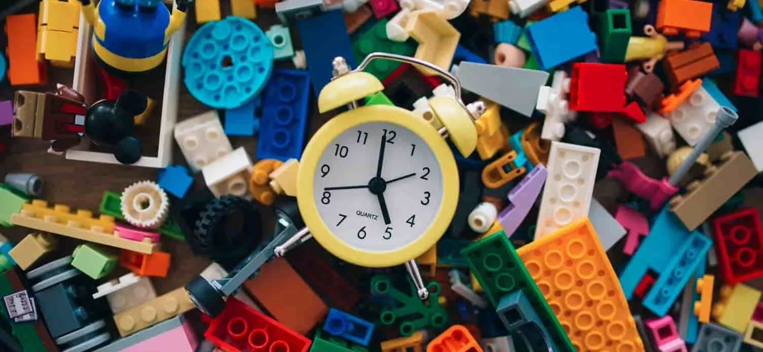 A vibrant assortment of building blocks and toys scattered across a table, featuring a bright yellow clock