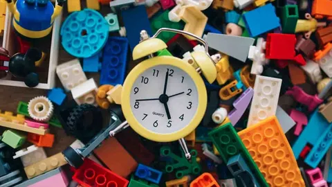 A vibrant assortment of building blocks and toys scattered across a table, featuring a bright yellow clock