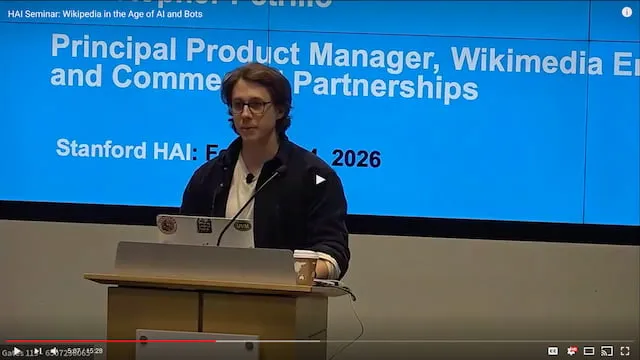 Video thumbnail: Christopher Petrillo speaking at a lectern in front of a slide titled Wikipedia in the Age of AI and Bots, Stanford HAI, February 4, 2026.
