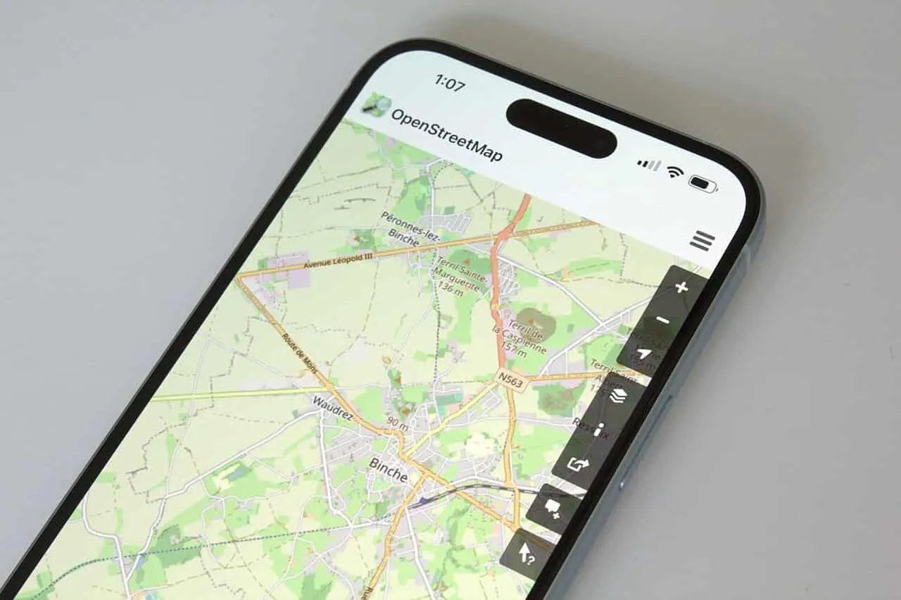 A closeup photograph of the top half of a phone, with the OpenStreetMap app open, focused on the city of Binche.