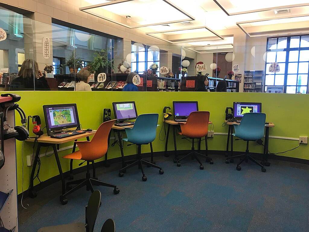 a colourful computer room for kids, with orange and blue chairs and a lime green wall against which are multiple computer screens.